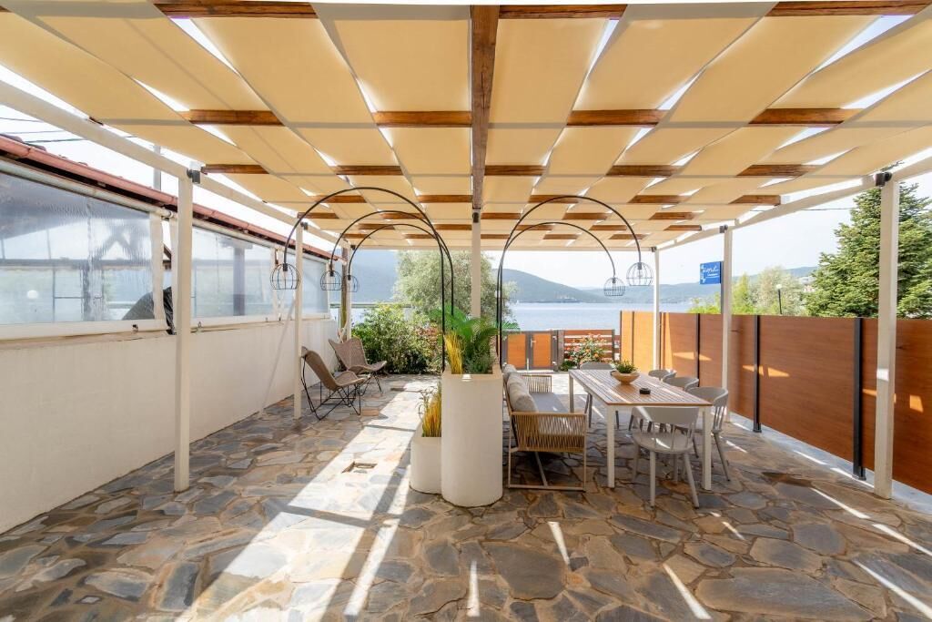 An outdoor patio with stone flooring, a table with chairs, and a view of the sea.