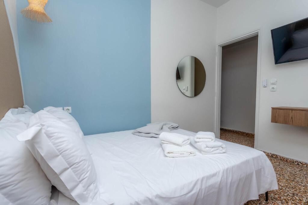 Una camera d'albergo con un letto, lenzuola bianche, uno specchio rotondo, una televisione e uno scaffale in legno.
