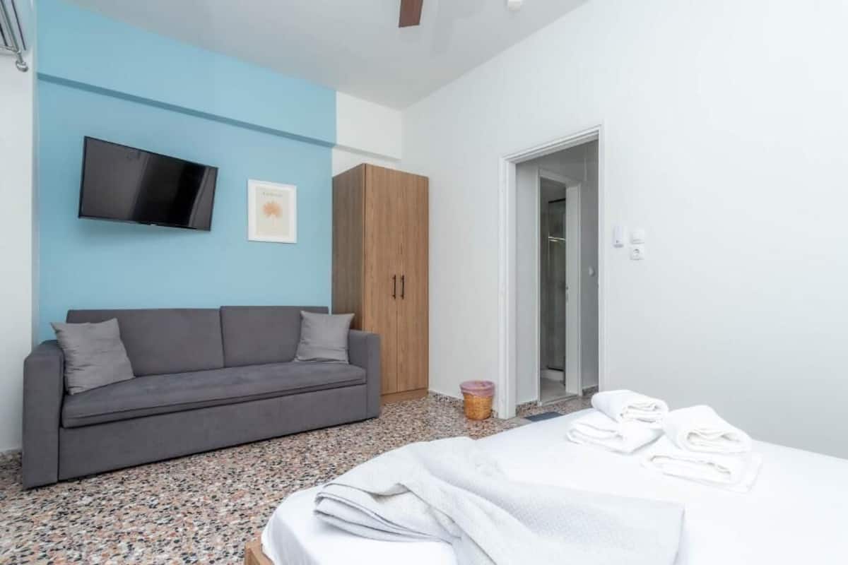 A bedroom with a bed, a grey sofa, a television on the wall, and a wardrobe.