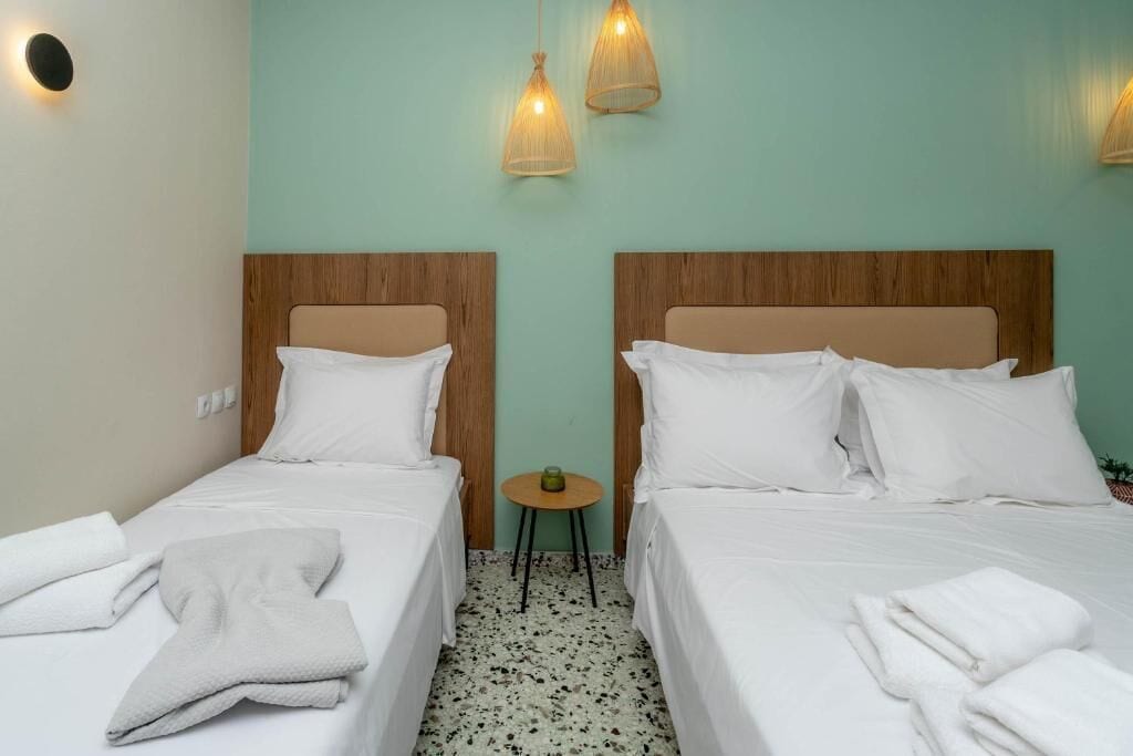 A hotel room with two beds, each with a wooden headboard, white bedding, and a small round table between them.