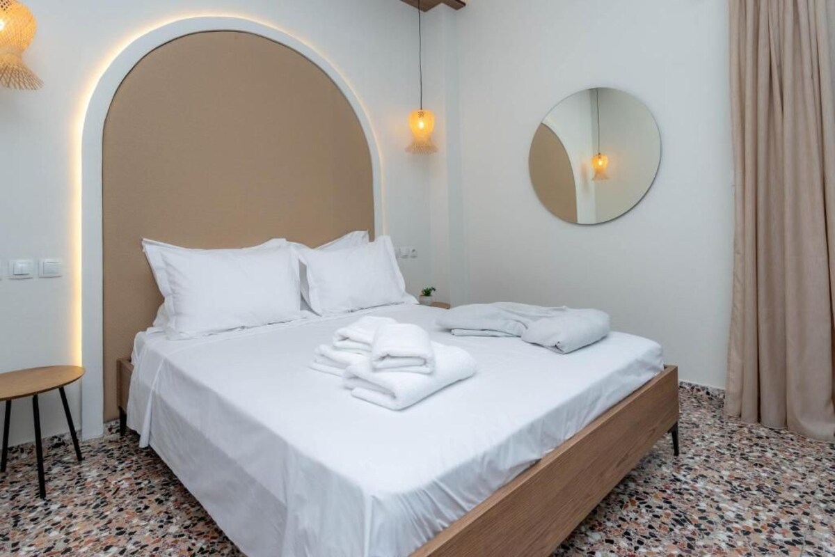 A neatly made bed with white linens and towels, a round mirror on the wall, and a small bedside table.