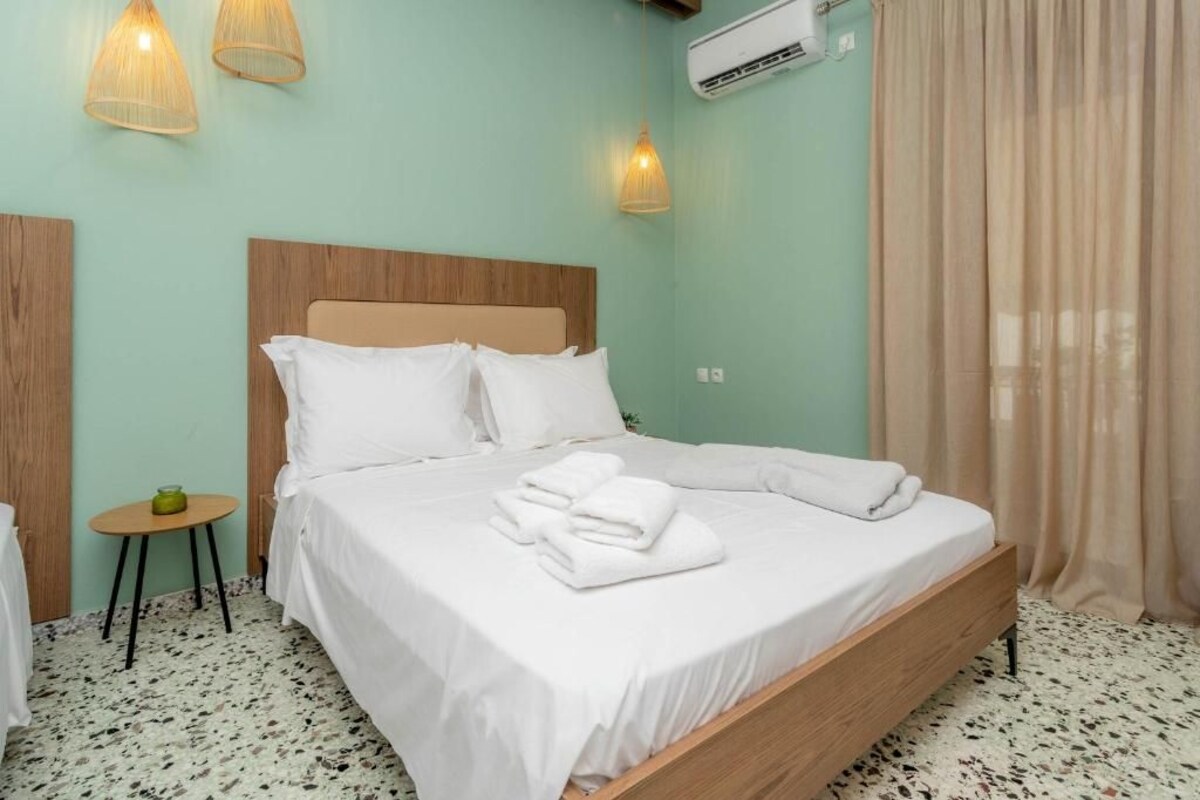 A neatly made bed with white linens and towels, a small round table with a green object, and a wall-mounted air conditioner.