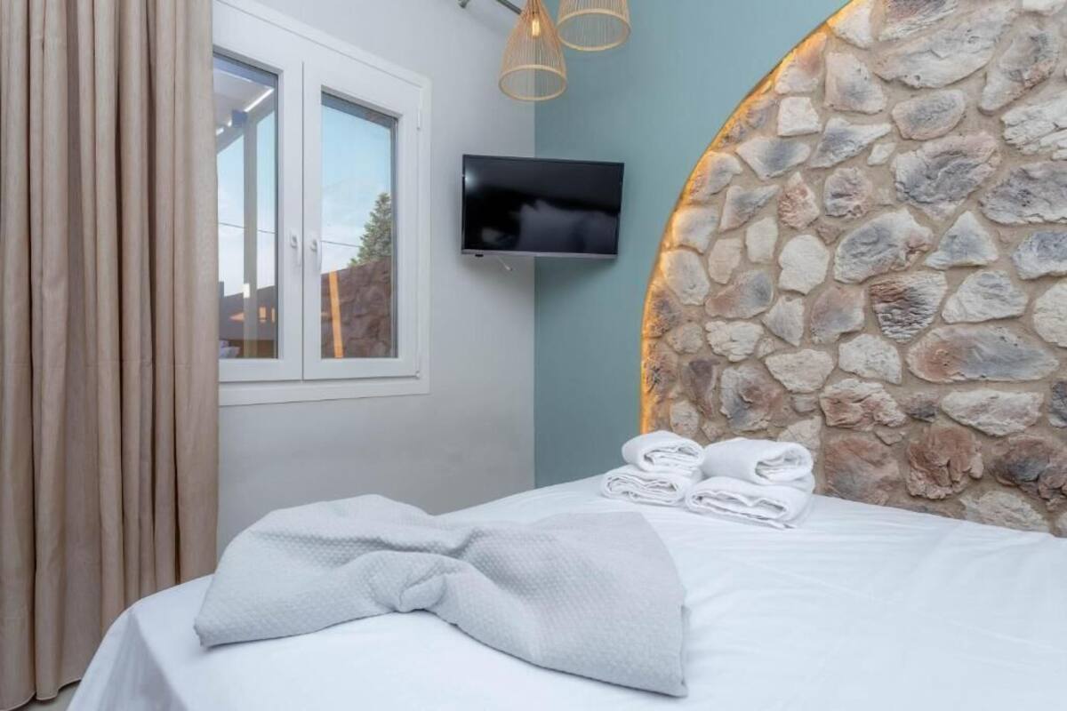 A bedroom with a stone headboard, a flat-screen TV, and a window with curtains.
