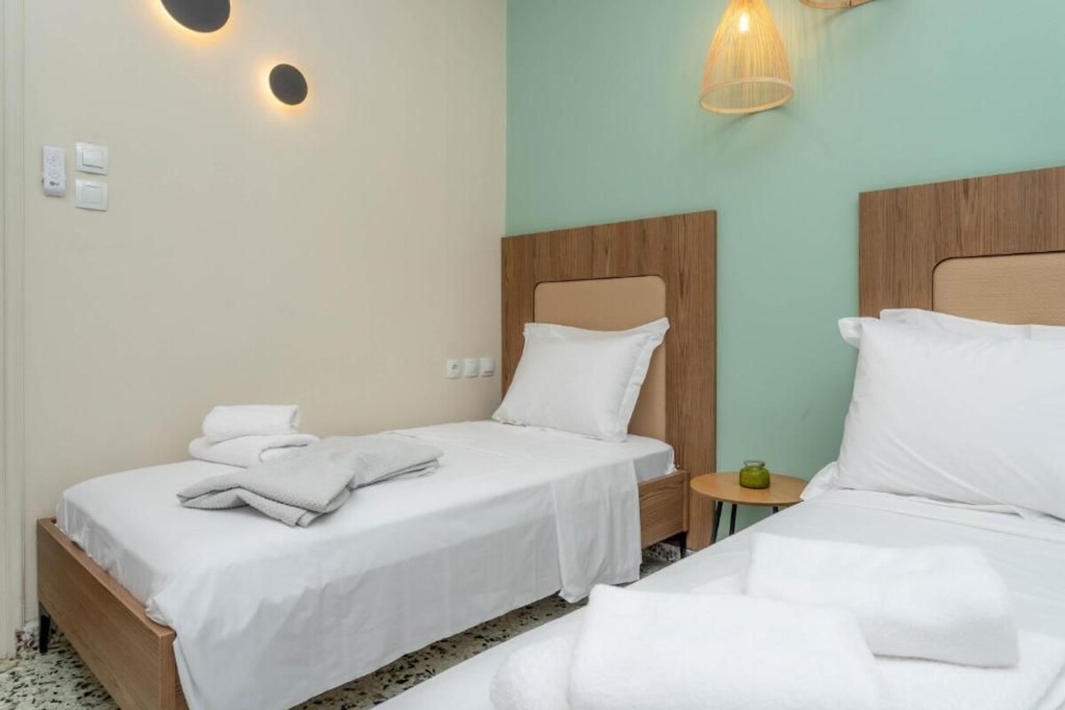Ein Hotelzimmer mit zwei Einzelbetten, einem kleinen Nachttisch mit Lampe sowie einer Wandleuchte.