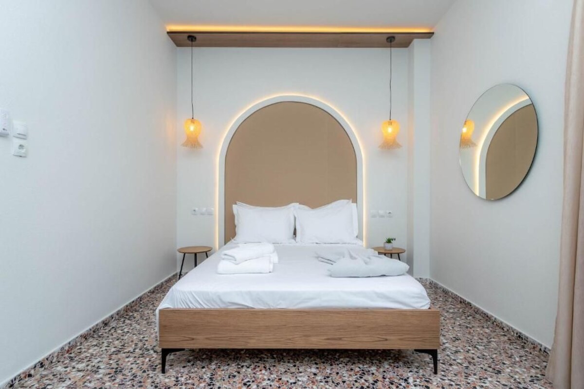 A modern bedroom with a wooden bed, white linens, a round mirror, and two bedside lamps.