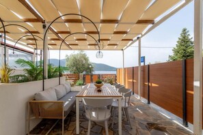 An outdoor patio with a wooden table and chairs, a sofa, and a pergola with hanging lights. - Pteleo apartments (Almyros)