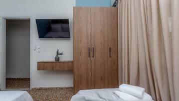 Une chambre à coucher avec un lit, une armoire en bois, un téléviseur fixé au mur et une petite étagère avec une plante.