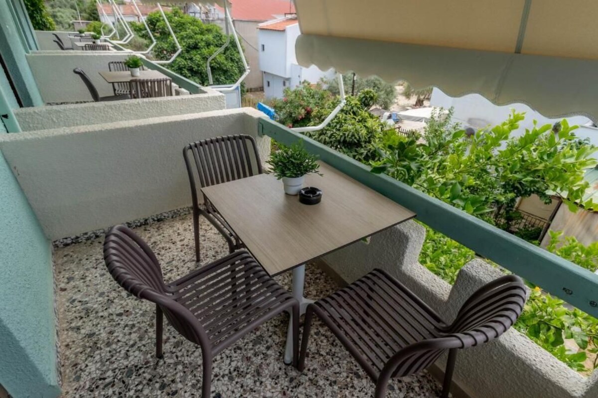 A balcony with a table and two chairs, a potted plant, and a view of greenery and buildings.