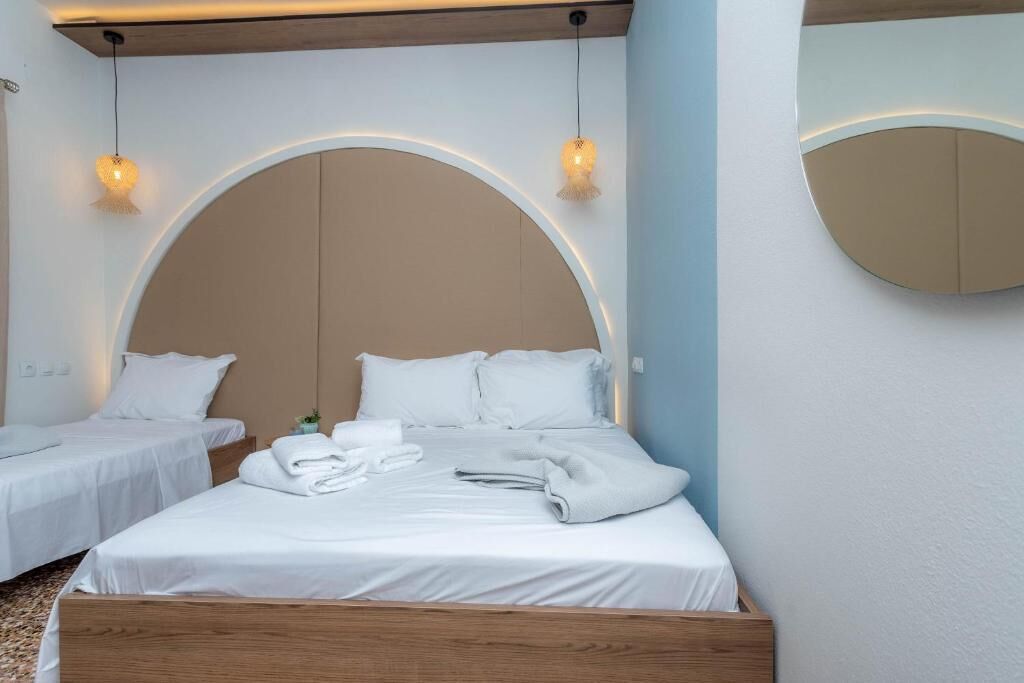 Hotellihuone, jossa on suuri sänky, kaksi pienempää sänkyä, puinen pääty ja kaksi riippuvalaisinta.