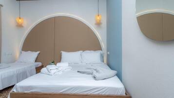 Hotellihuone, jossa on suuri sänky, kaksi pienempää sänkyä, puinen pääty ja kaksi riippuvalaisinta.