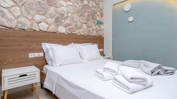 A neatly made bed with white linens and pillows, a stone wall, and a nightstand with a lamp.