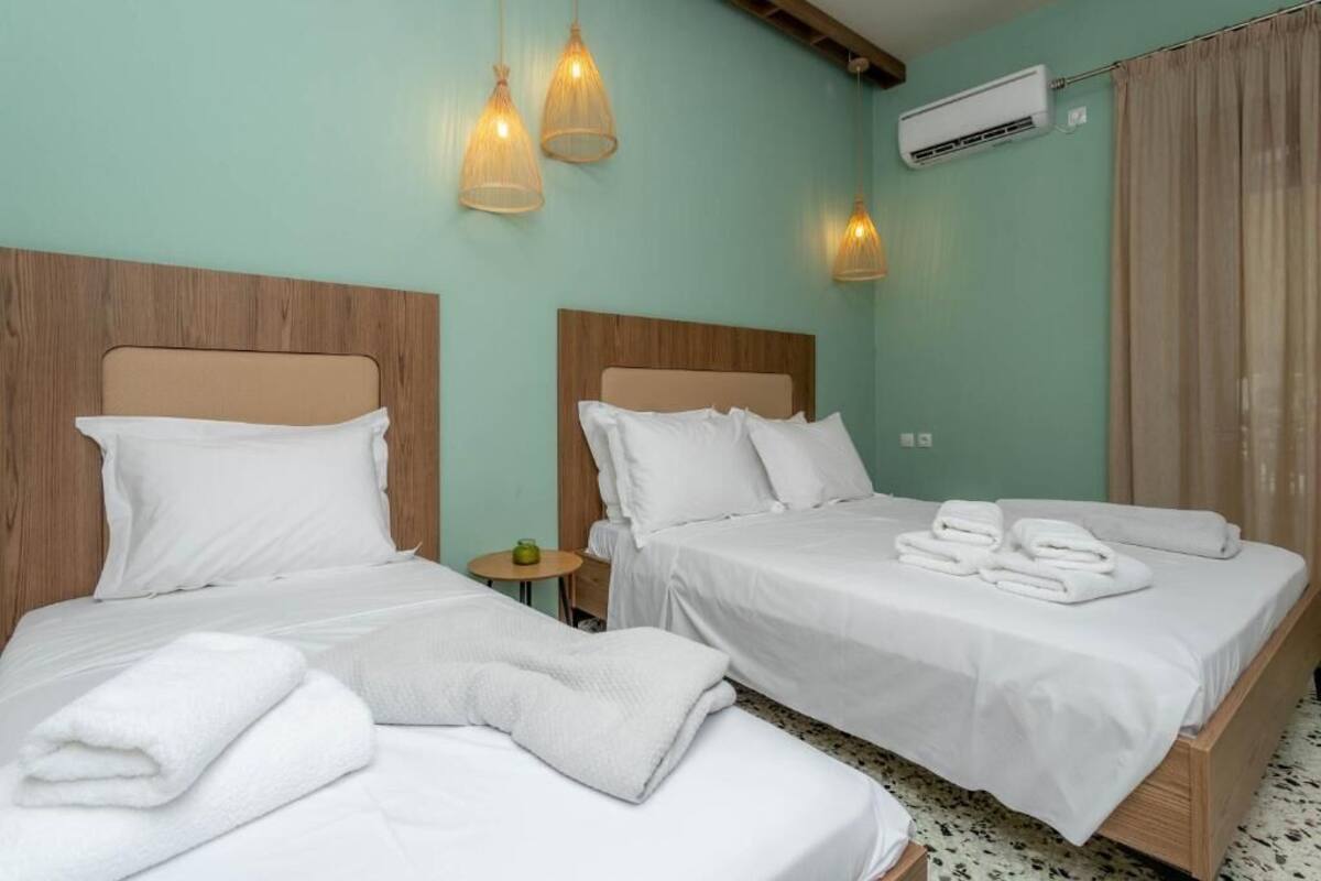 A hotel room with two beds, a small table, and a wall-mounted air conditioner.
