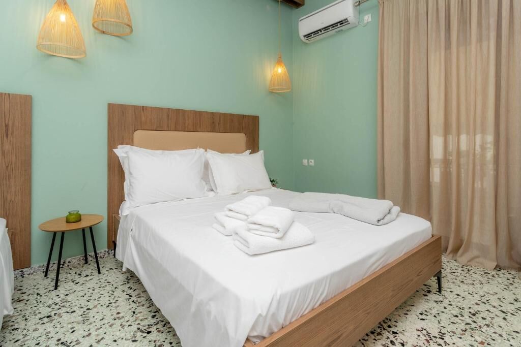 A neatly made bed with white linens and towels, a small round table with a green object, and a wall-mounted air conditioner.