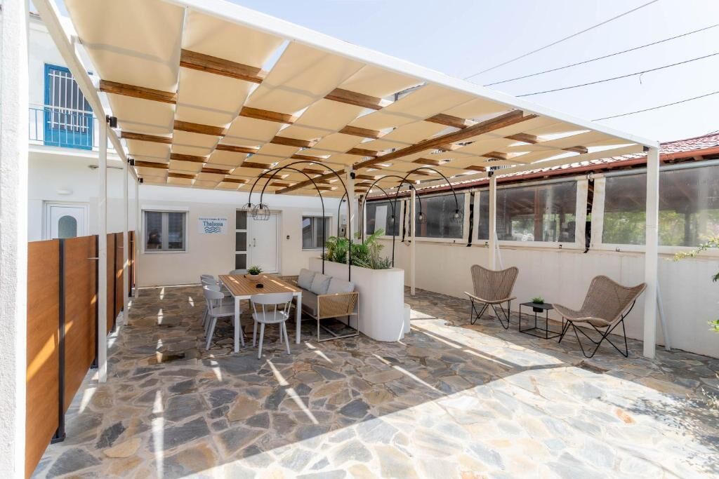 A covered outdoor patio with stone flooring, a wooden table, and seating.