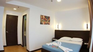 Quarto de hotel com cama, porta, quadro e mesa de cabeceira.