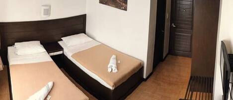 A hotel room with two single beds, a wooden floor, a painting on the wall, and a door.