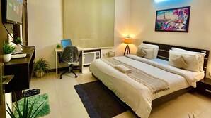 Une chambre d’hôtel avec un lit, un bureau, une chaise, des plantes en pot et un tableau au mur.