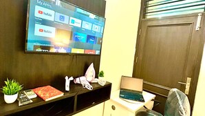 Un espace de bureau moderne doté d’un téléviseur fixé au mur qui affiche différentes applications, d’un bureau avec un ordinateur portable, d’une chaise et de deux plantes en pot.