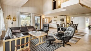 A spacious living area with a high ceiling, wooden walls, a dining area, and a kitchen.