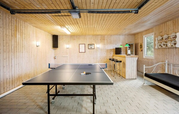 Une table de ping-pong dans une pièce aux murs en bois et au sol en briques.