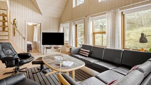 A modern living room with a large TV, leather sofa, and a dining area with a table and chairs.