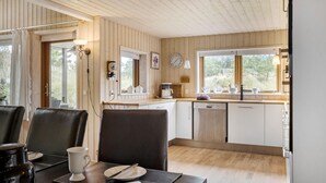 A cozy kitchen with wooden walls, a dining area with chairs, a coffee maker, and a clock on the wall.