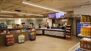 Ein Supermarktfass mit einer zentralen Theke, Regalen voller Snacks und einer Kühltheke rechts.