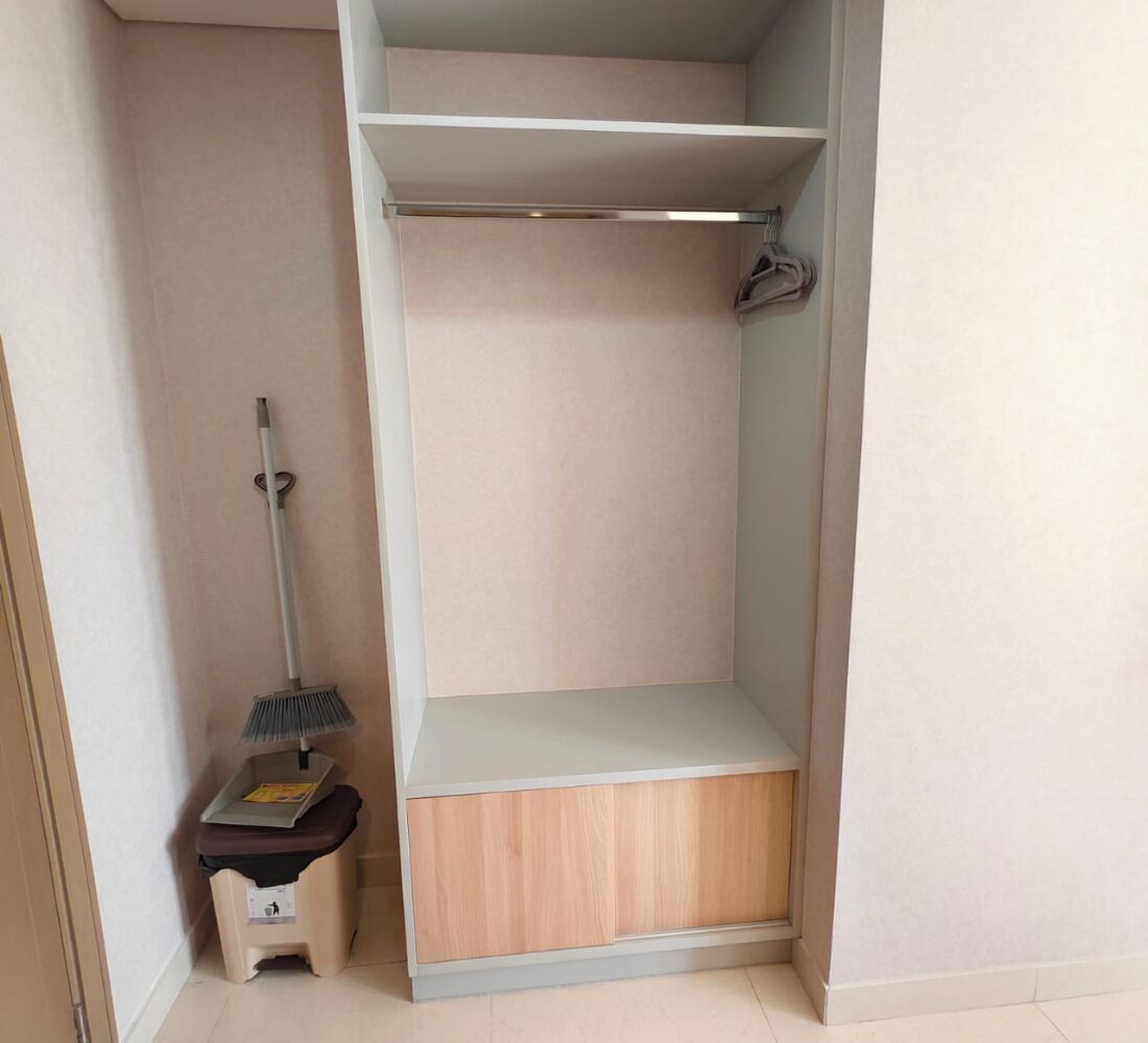 Un placard avec une étagère inférieure en bois, une tringle métallique pour suspendre les vêtements et un balai appuyé contre le mur.