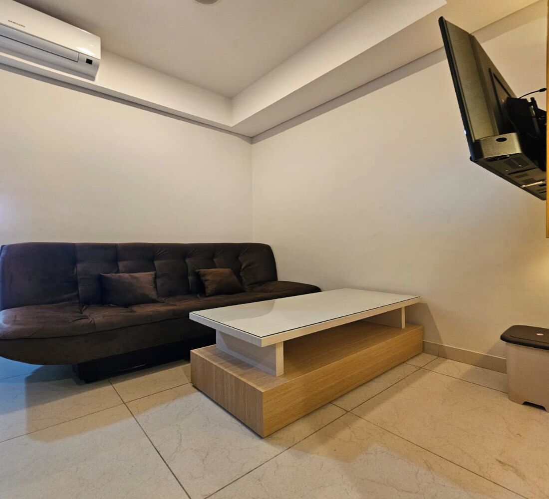 Una sala de estar moderna con un sofá marrón oscuro, una mesa de centro blanca y un televisor de pantalla plana montado en la pared.