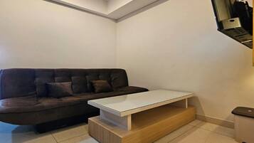 Una sala de estar moderna con un sofá marrón oscuro, una mesa de centro blanca y un televisor de pantalla plana montado en la pared.