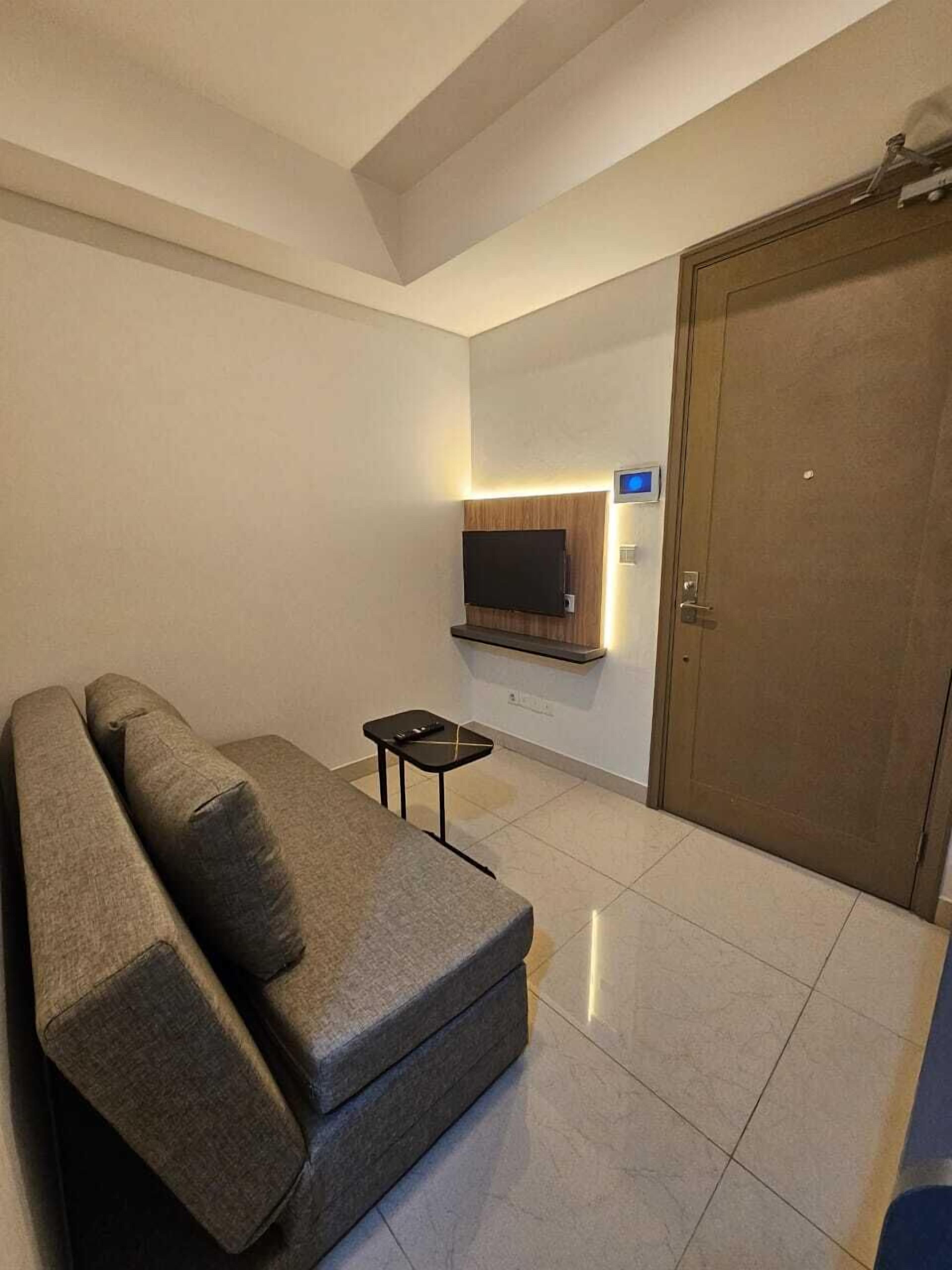 A modern living room with a grey sofa, a small black side table, and a flat-screen TV mounted on the wall.