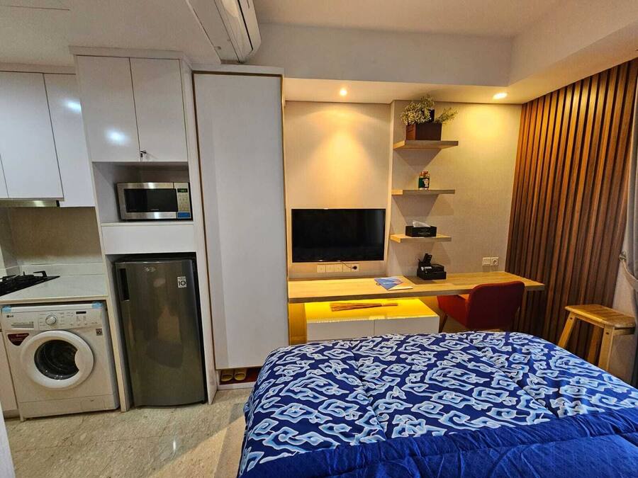 A compact hotel room with a bed, a desk with a flat-screen TV, a washing machine, and a microwave.