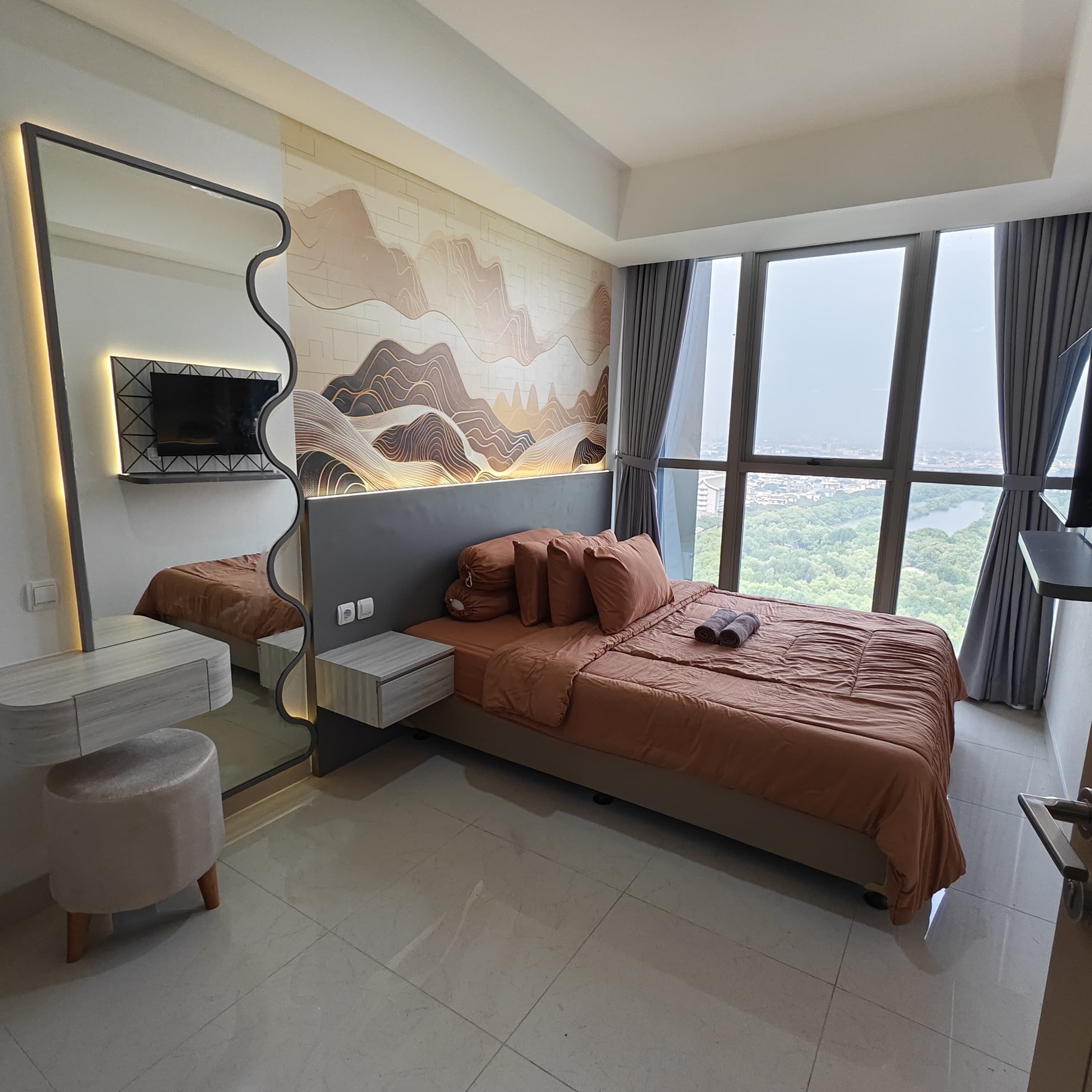 A modern bedroom with a large bed, a bedside table, a mirror, and a TV mounted on the wall.
