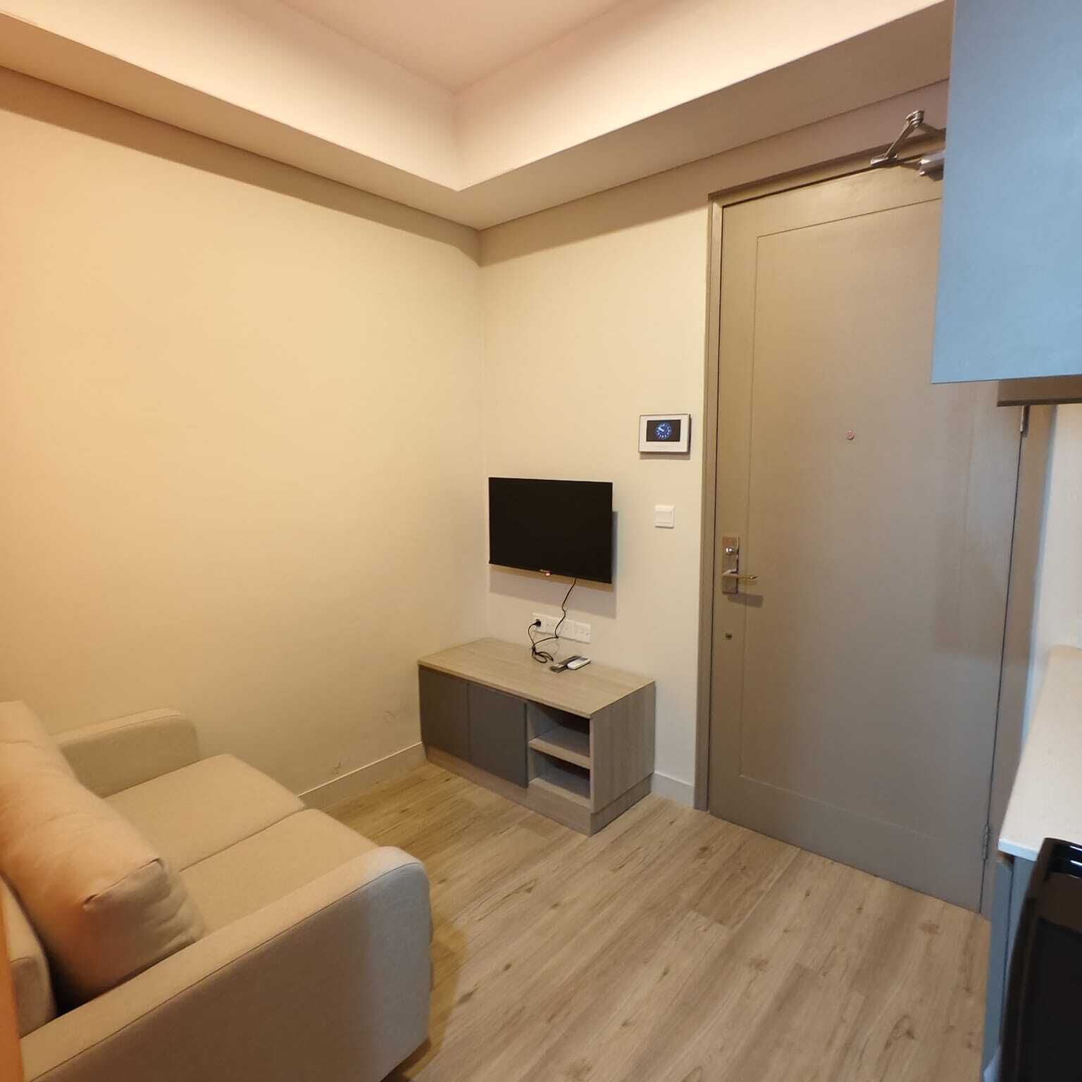 Una sala de estar moderna con un televisor de pantalla plana montado en la pared, un mueble de madera debajo y un sofá color beige.