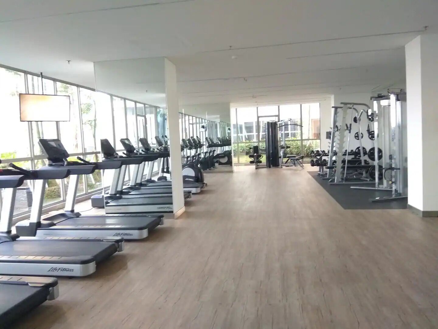 Een fitnessruimte met loopbanden, krachttoestellen en een ruim venstergedeelte.