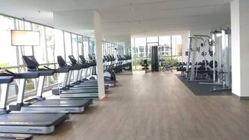 Een fitnessruimte met loopbanden, krachttoestellen en een ruim venstergedeelte.