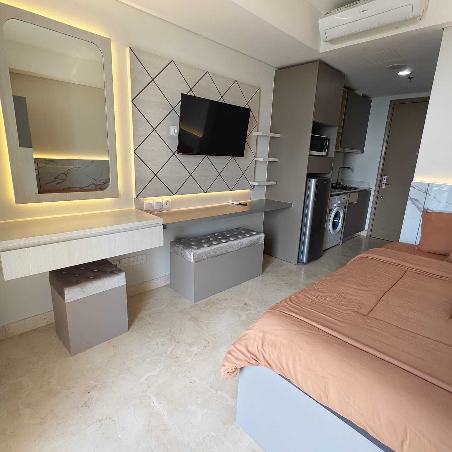 A modern bedroom with a bed, a TV, a washing machine, and a small kitchenette.