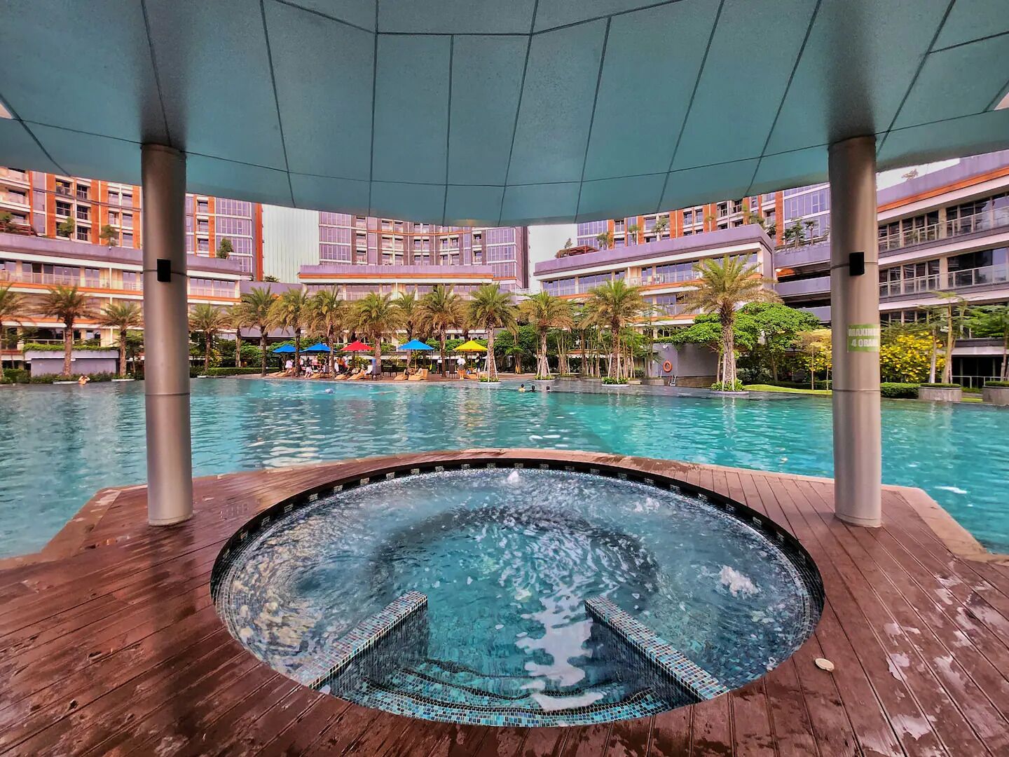 Ein Poolbereich eines Hotels mit Whirlpool, Holzterrasse und Blick auf die Hotelgebäude.