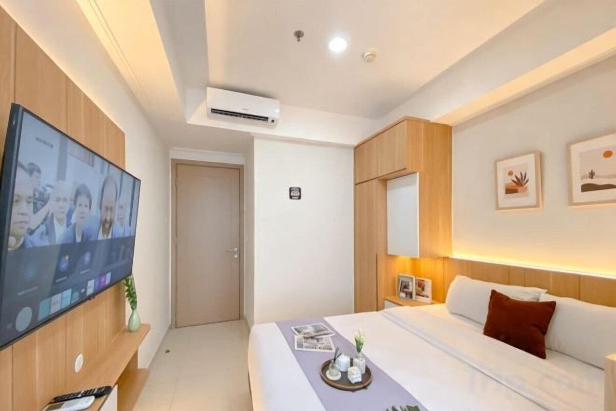 A hotel room with a bed, a TV mounted on the wall, a door, and a wall-mounted air conditioner.