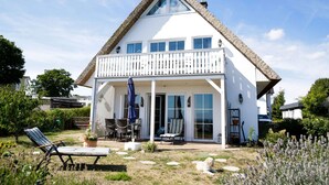 A white house with a thatched roof, a balcony, and a patio area with outdoor furniture.