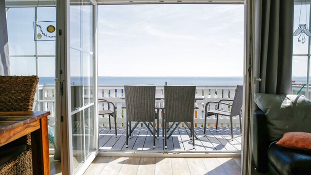 En balkon med fletmøbler, udsigt til havet og en glasdør, der fører ind.