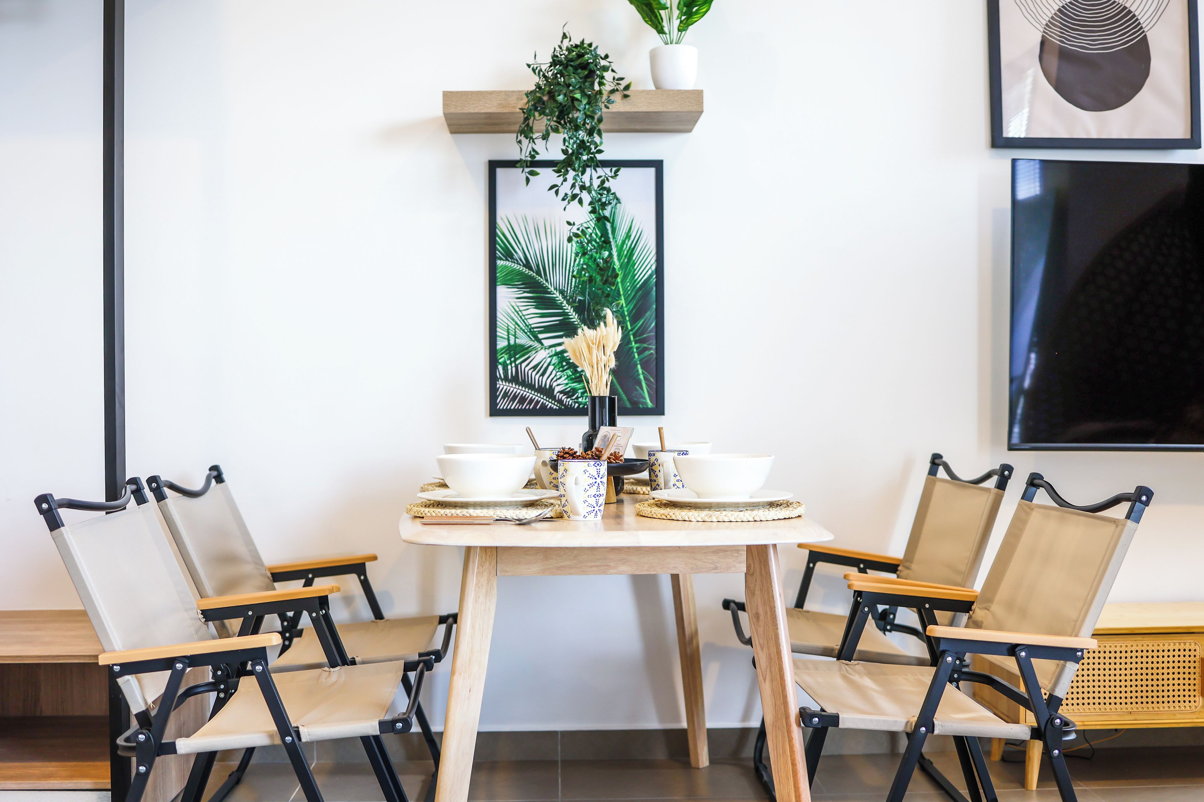 Un comedor con una mesa de madera, cuatro sillas y una planta en maceta sobre una estantería.