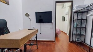 Ein Zimmer mit einem Holztisch, einem Stuhl, einem an der Wand befestigten Fernseher und einer Metallregaleinheit.