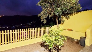 Ein Außenbereich bei Nacht mit einem kleinen Baum, einer gelben Wand und einem weißen Zaun.