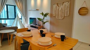A dining area with a wooden table set for four, a sofa, and a TV in the background. - The Horizon by MyKey (Ipoh)