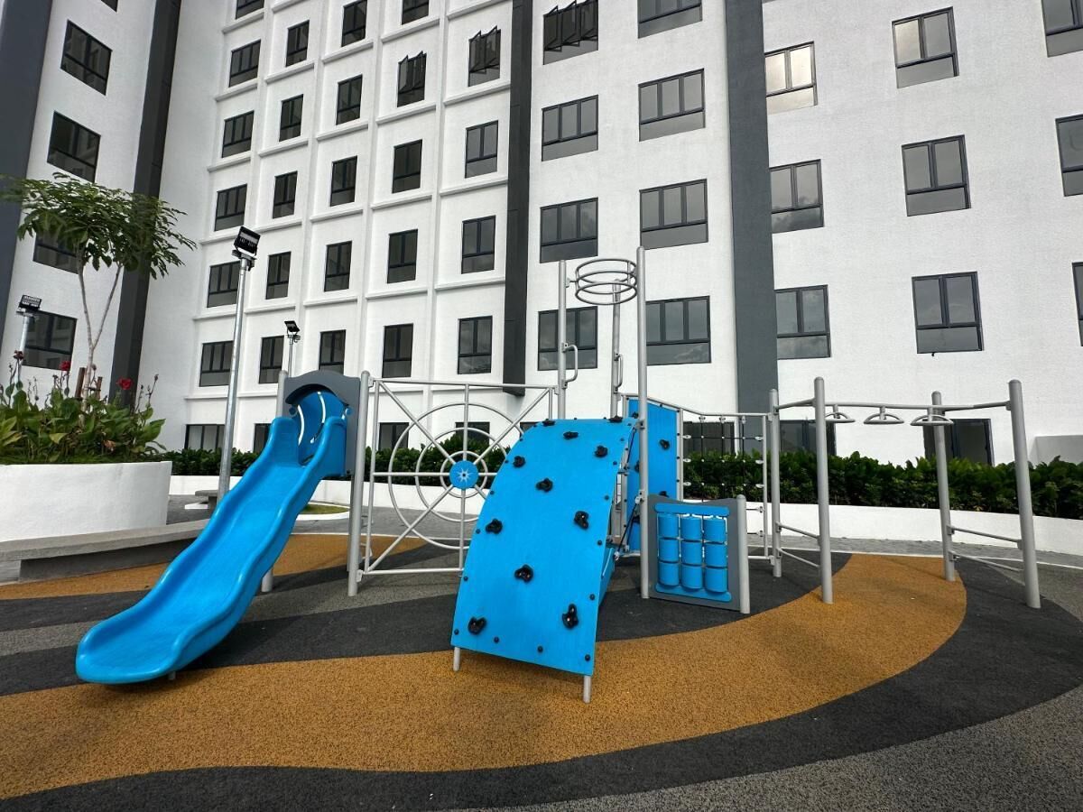 Un terrain de jeux avec un toboggan bleu et des structures d’escalade, situé devant la façade d’un bâtiment moderne.