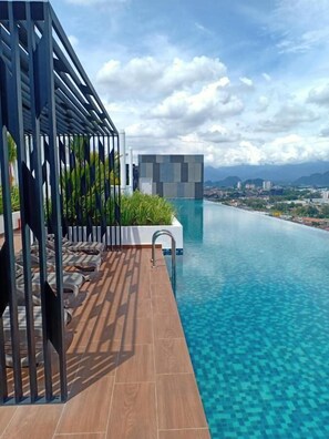 Ein Pool ohne Rand mit einer Holzterrasse und einem modernen Gebäude im Hintergrund.