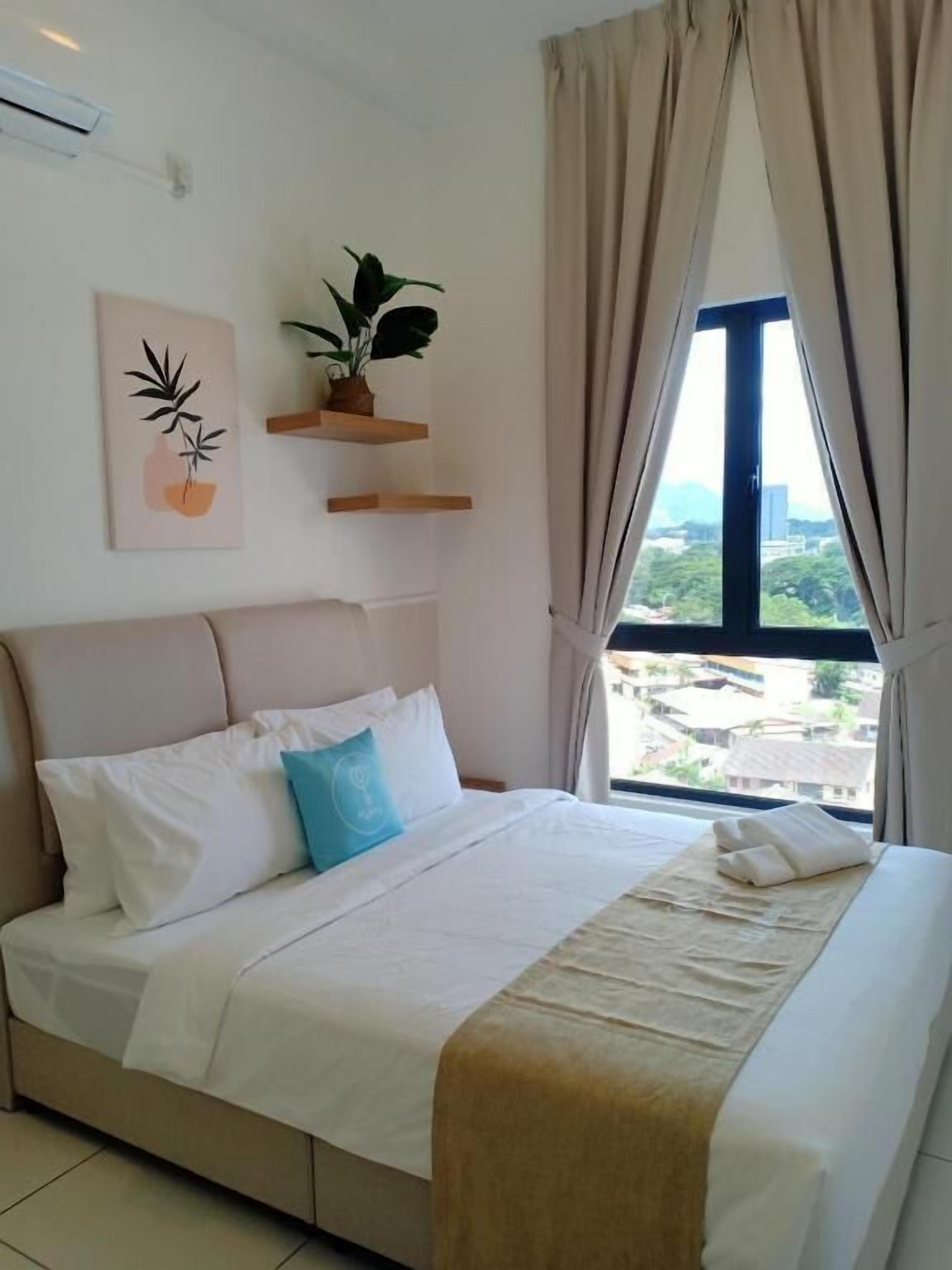 A neatly made bed with white bedding and a blue pillow, a potted plant on a wooden shelf, and a window with curtains.