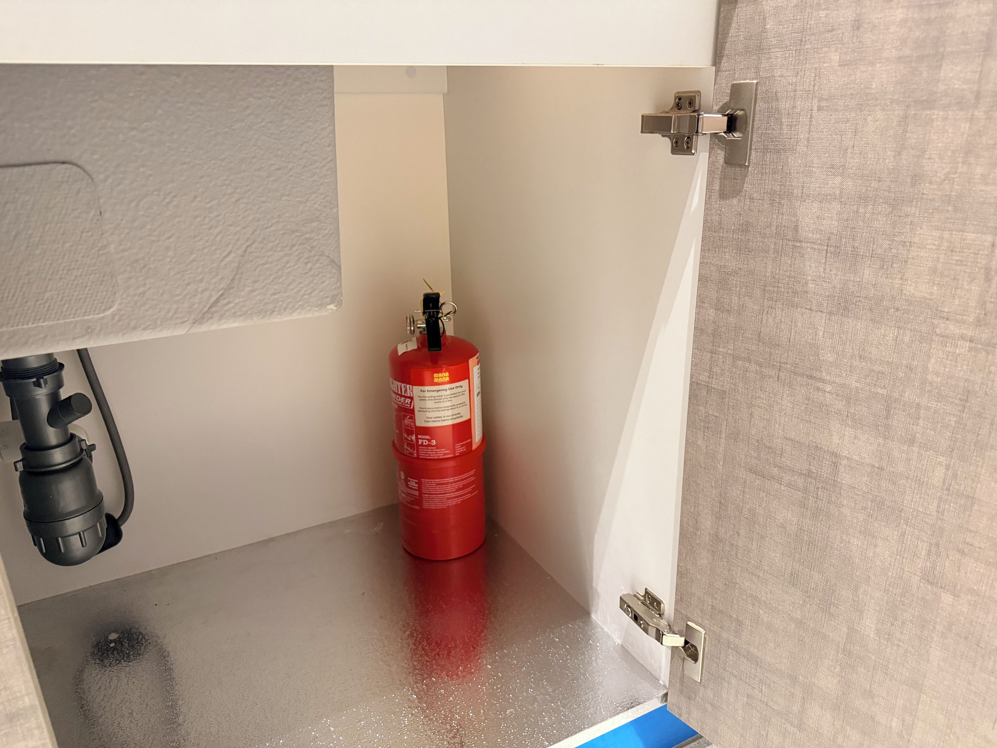 Un extintor rojo fijado a una pared, una bisagra de metal de una puerta y una manguera negra.