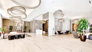 Een ruime lobby met een modern design, met een centraal zithoekje met lederen stoelen, een receptiebalie en decoratieve verlichting.